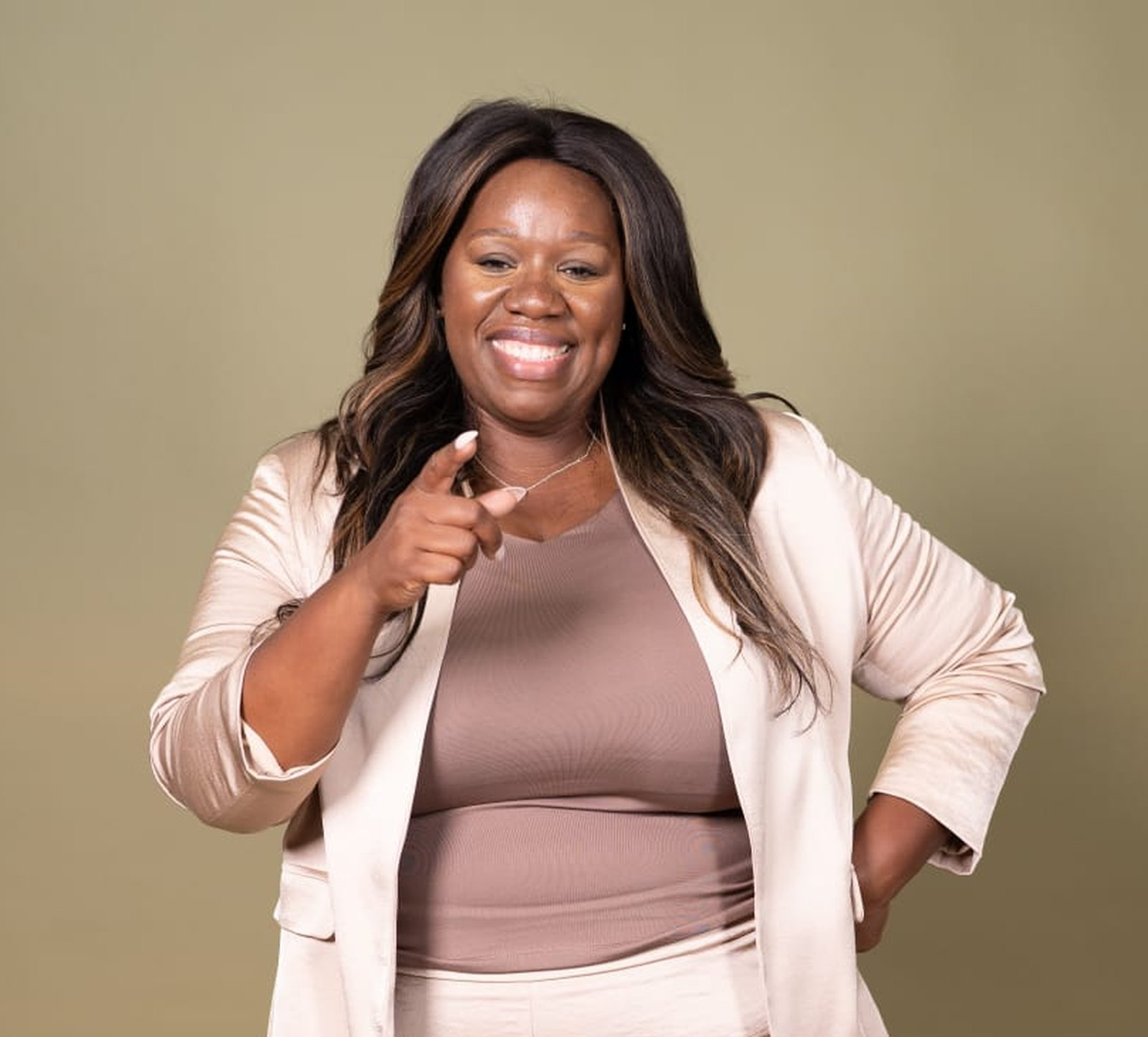 Nadea Clarke smiling and pointing towards the camera, wearing a cream suit.